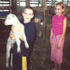 Brother holds lamb while sister looks on.