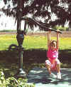 Girl hangs from the handle of a water pump.