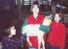 One sister holds the lamb while the other two pet it.